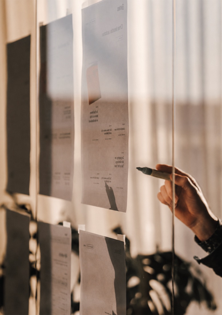 Feuilles de travail affichées sur une vitre, annotées au feutre