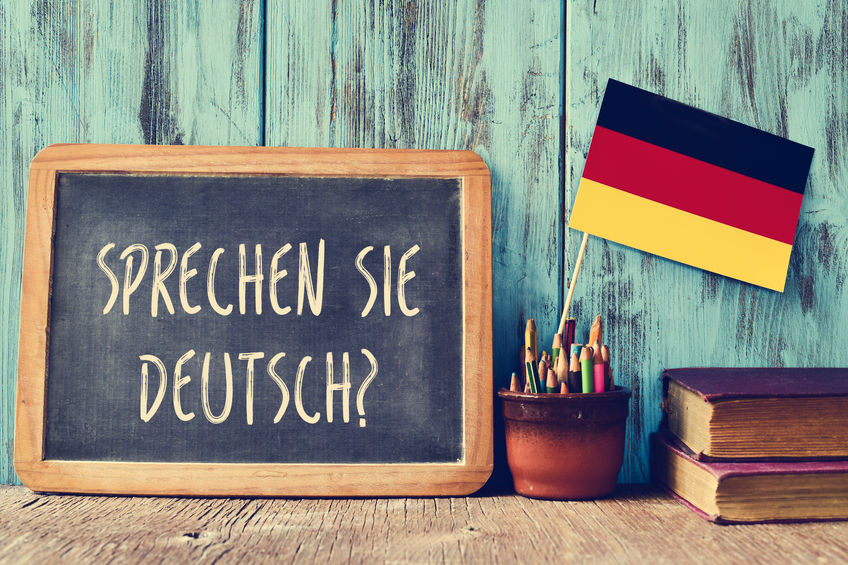 question sprechen sie deutsch? do you speak german? a chalkboard with the question sprechen sie deutsch? do you speak german? written in german, a pot with pencils, some books and the flag of Germany, on a wooden desk