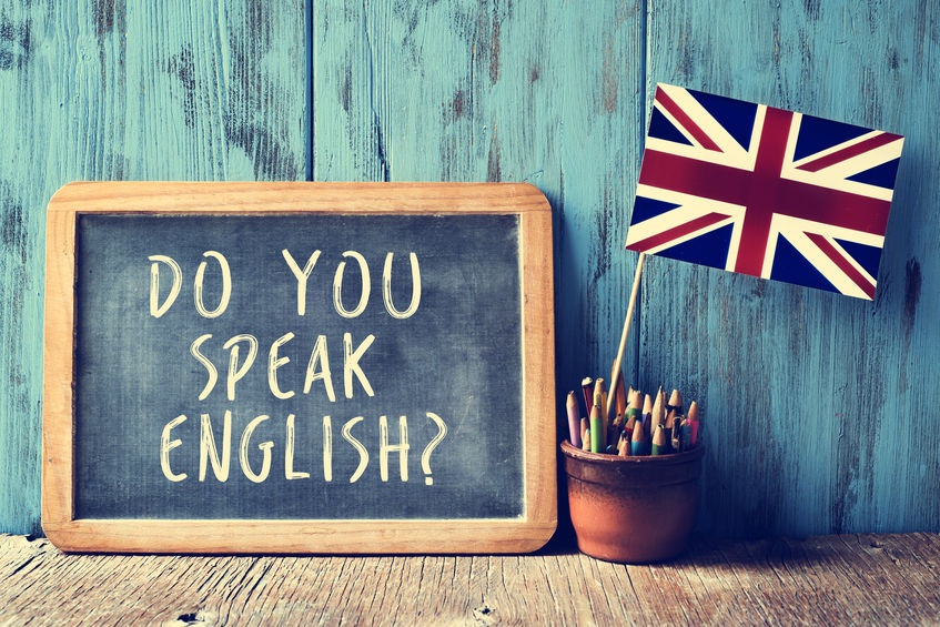 text do you speak english? in a chalkboard, filtered a chalkboard with the text do you speak english? written in it, a pot with pencils and the flag of the United Kingdom, on a wooden desk, with a filter effect