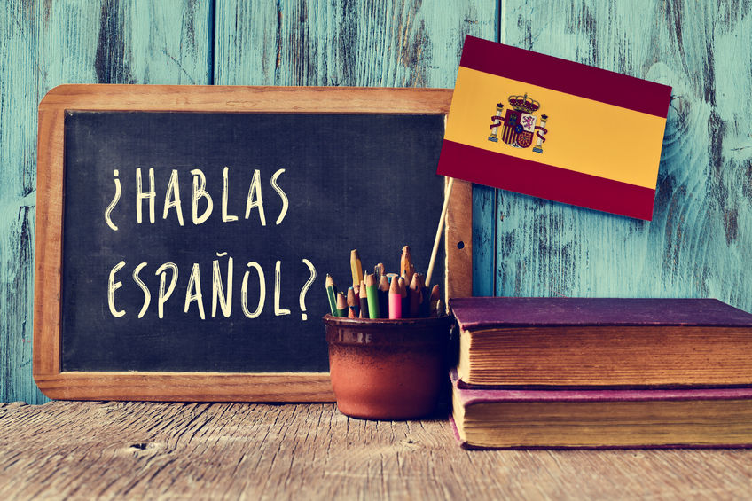 46738484 - a chalkboard with the question hablas espanol? do you speak spanish? written in spanish, a pot with pencils and the flag of spain, on a wooden desk