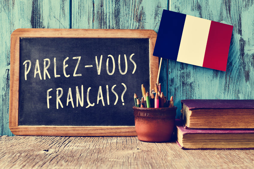 Francais 46480434 - a chalkboard with the question parlez-vous francais? do you speak french? written in french, a pot with pencils and the flag of france, on a wooden desk
