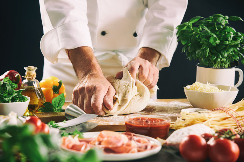 Chef kneading pastry dough for pasta or pizza in a close up view of his hands and assorted fresh ingredients